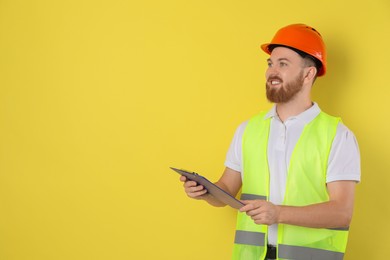 Photo of Engineer in hard hat with clipboard on yellow background, space for text