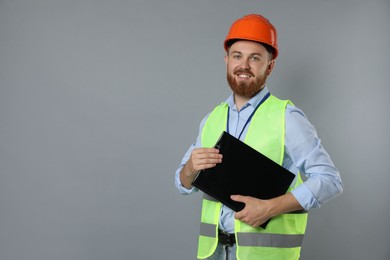 Engineer in hard hat with clipboard on grey background, space for text