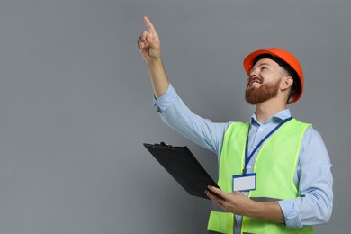 Photo of Engineer in hard hat with clipboard on grey background, space for text