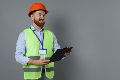 Photo of Engineer in hard hat with clipboard on grey background, space for text