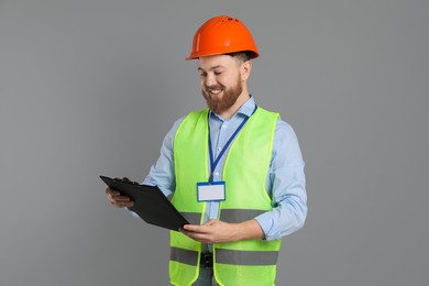 Engineer in hard hat with clipboard on grey background