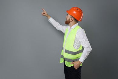 Photo of Engineer in hard hat pointing at something on grey background, space for text