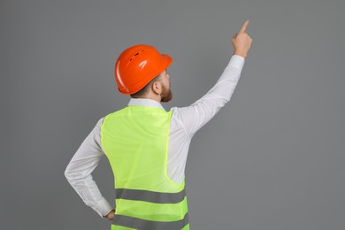 Engineer in hard hat pointing at something on grey background, space for text