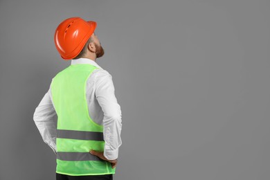 Engineer in hard hat on grey background, space for text