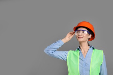 Photo of Engineer in hard hat and goggles on grey background, space for text