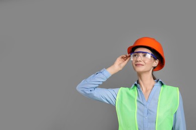 Engineer in hard hat and goggles on grey background, space for text