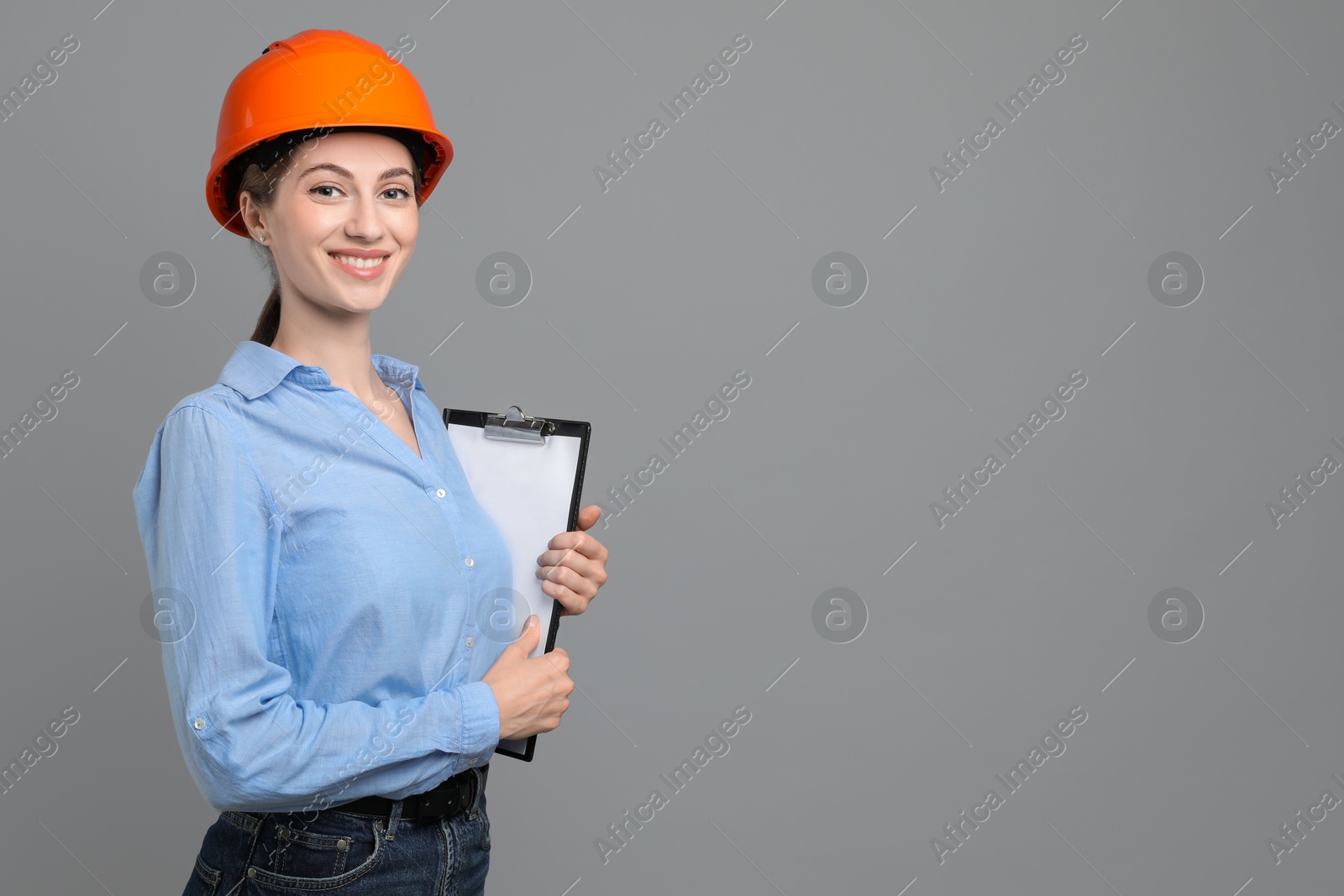 Photo of Engineer in hard hat with clipboard on grey background, space for text