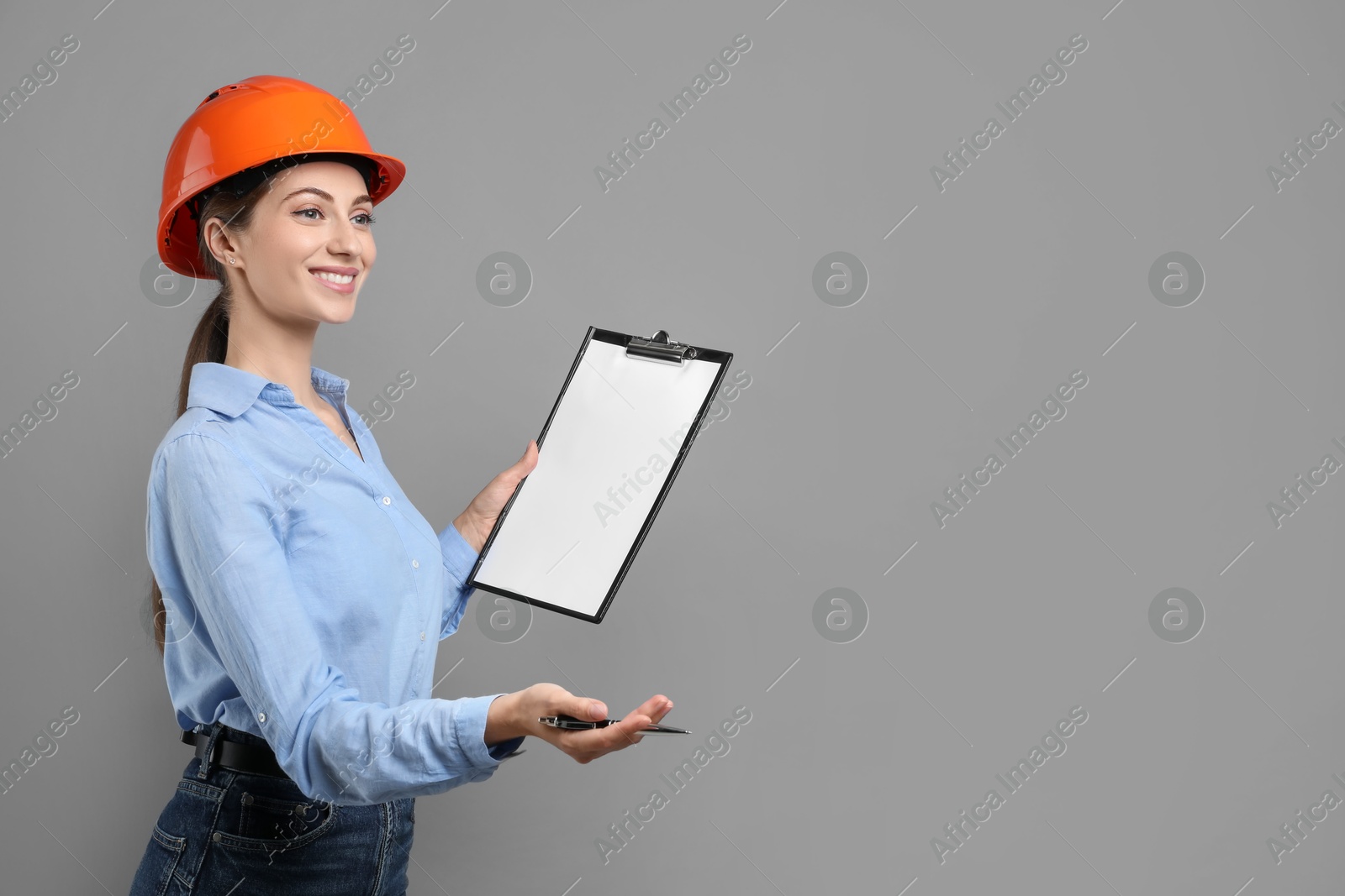 Photo of Engineer in hard hat with clipboard and pen on grey background, space for text