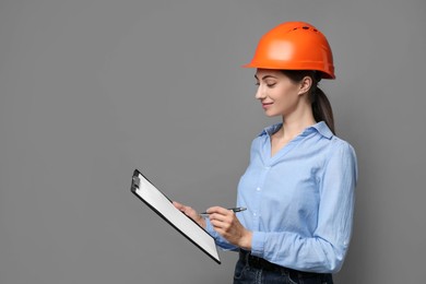 Engineer in hard hat with clipboard and pen on grey background, space for text