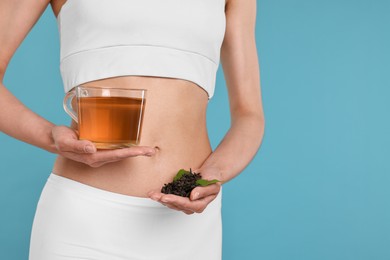 Photo of Weight loss concept. Woman with cup of diet tea and dry leaves on light blue background, closeup