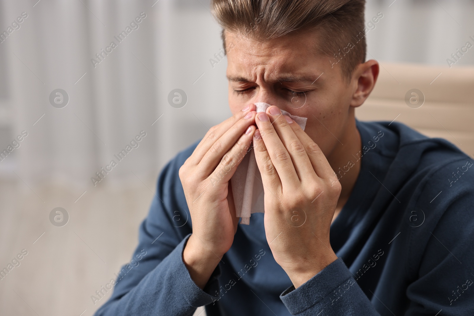 Photo of Young man with tissue suffering from sinusitis indoors, space for text