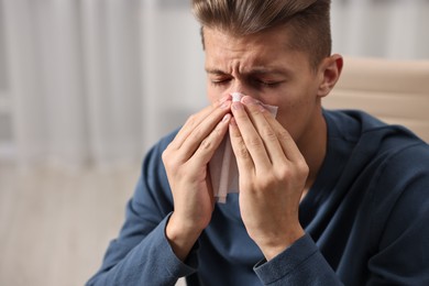 Young man with tissue suffering from sinusitis indoors, space for text