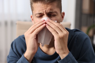 Young man with tissue suffering from sinusitis indoors