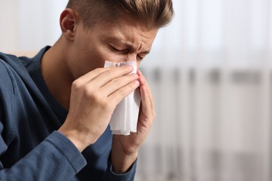 Photo of Young man with tissue suffering from sinusitis indoors, space for text