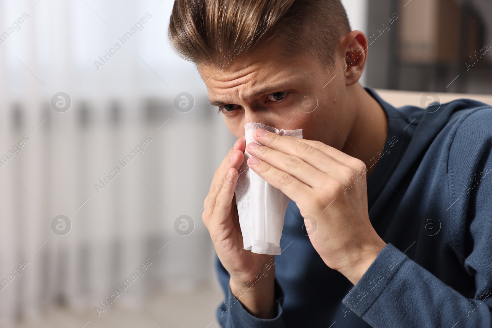 Photo of Young man with tissue suffering from sinusitis indoors, space for text