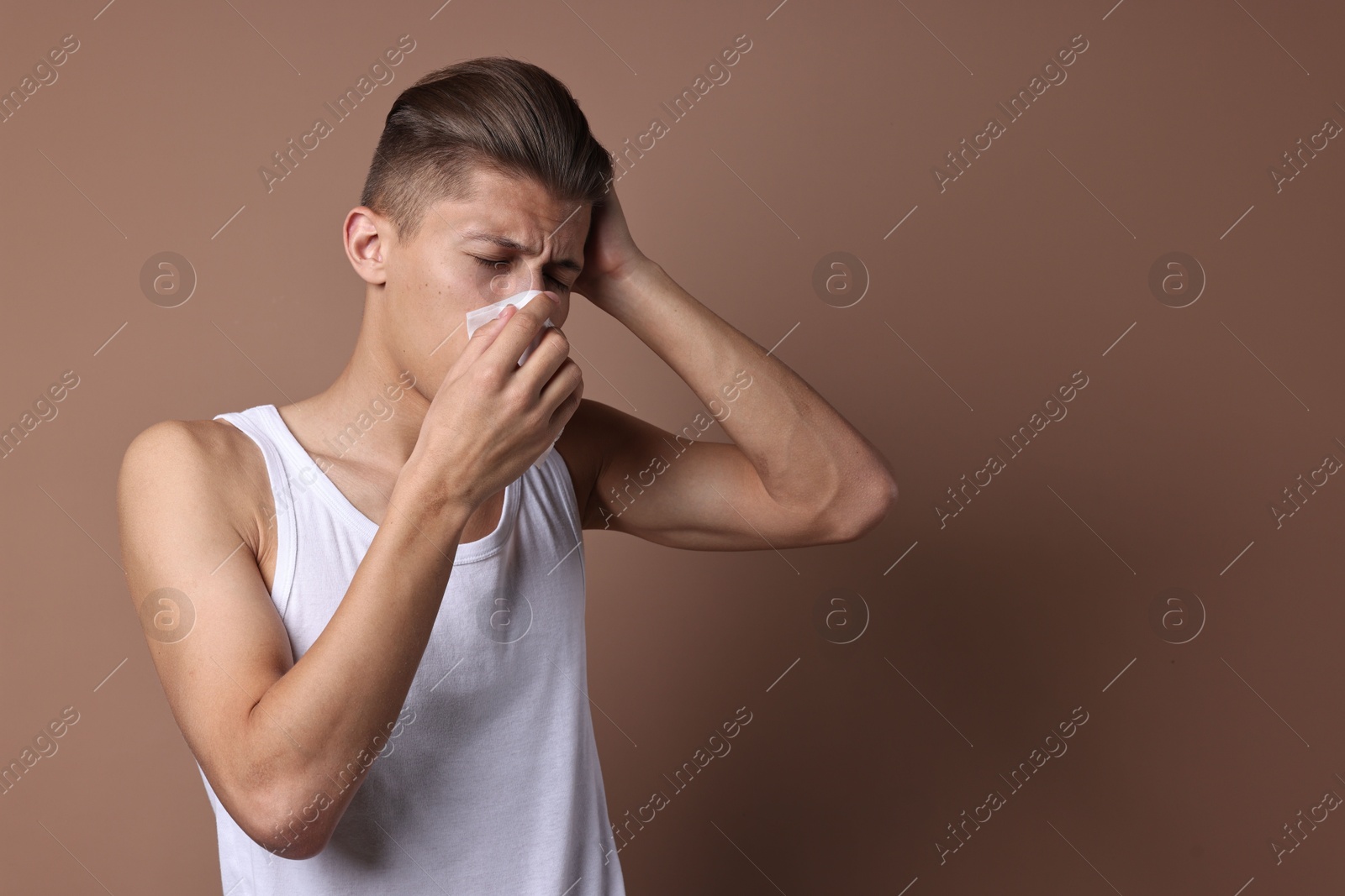 Photo of Young man with tissue suffering from sinusitis on light brown background, space for text