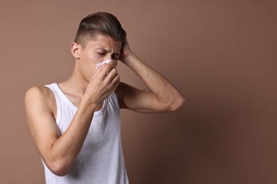 Young man with tissue suffering from sinusitis on light brown background, space for text