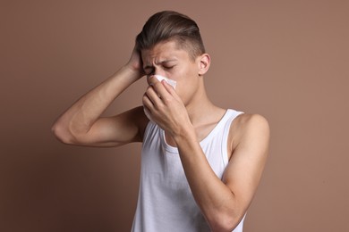 Photo of Young man with tissue suffering from sinusitis on light brown background