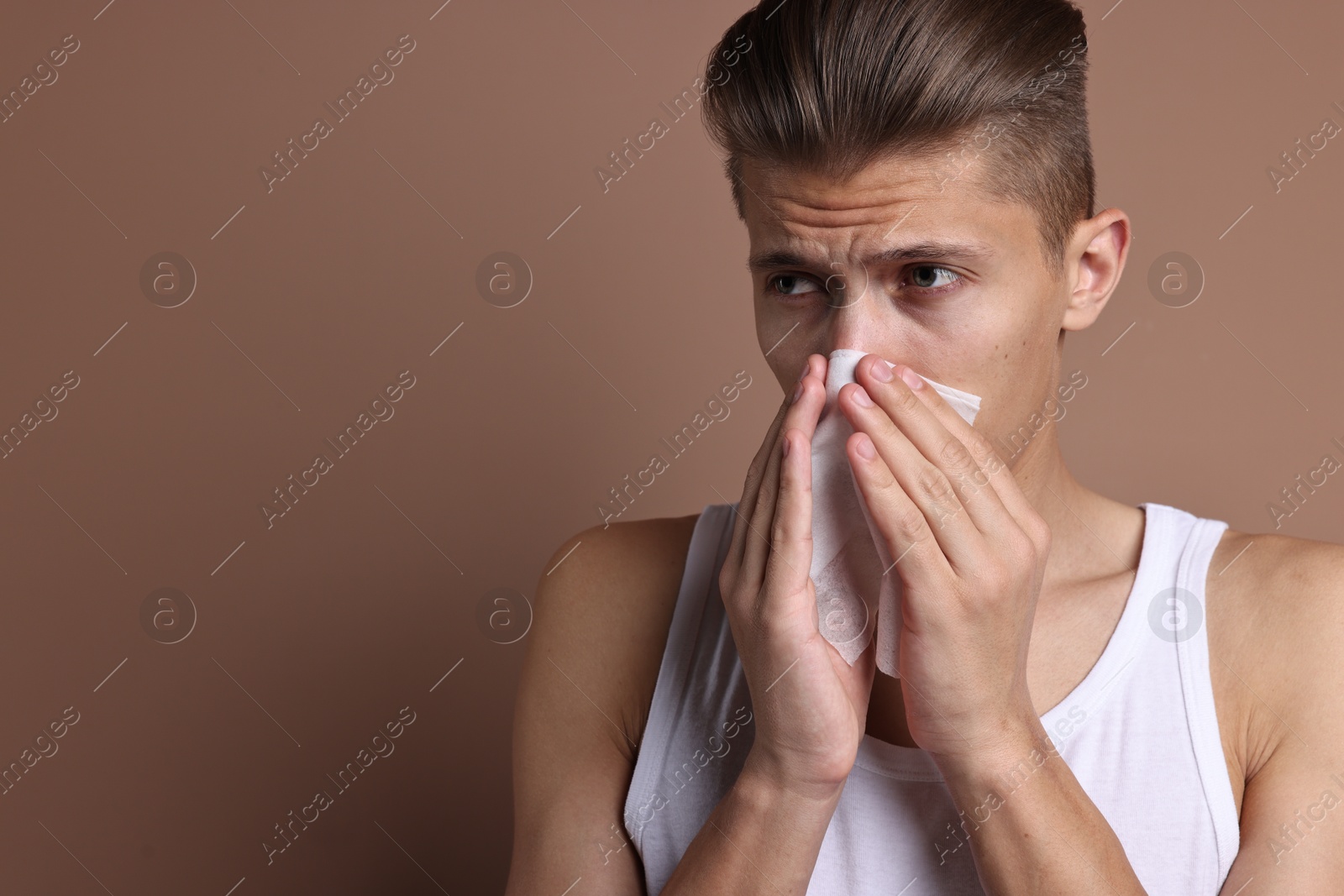 Photo of Young man with tissue suffering from sinusitis on light brown background, space for text