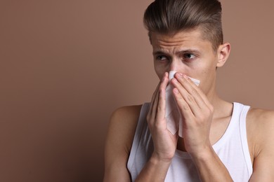 Photo of Young man with tissue suffering from sinusitis on light brown background, space for text