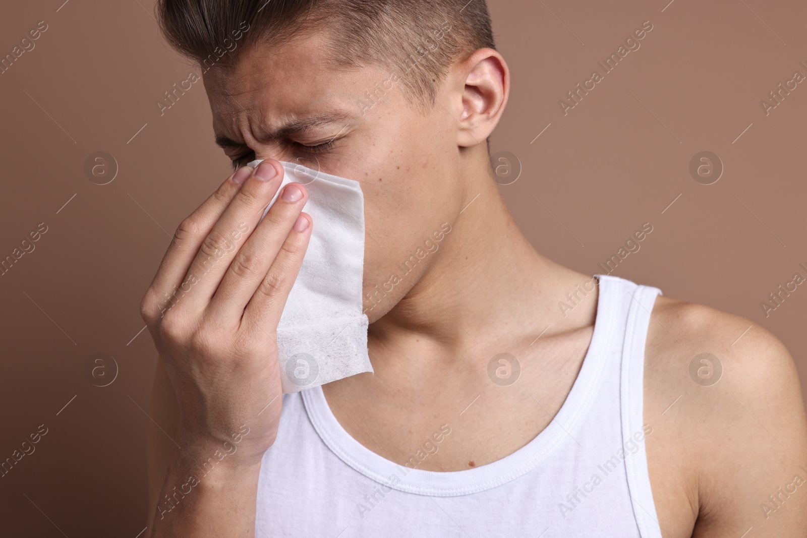 Photo of Young man with tissue suffering from sinusitis on light brown background