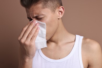 Photo of Young man with tissue suffering from sinusitis on light brown background