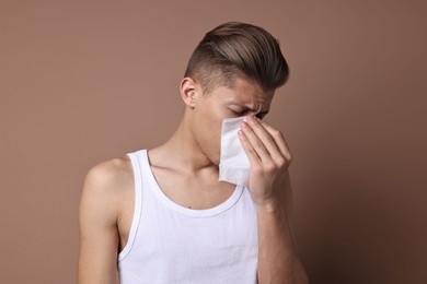 Photo of Young man with tissue suffering from sinusitis on light brown background