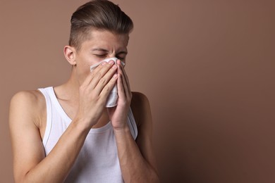 Photo of Young man with tissue suffering from sinusitis on light brown background, space for text