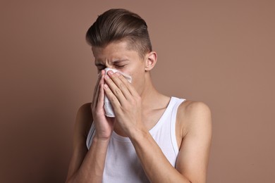 Young man with tissue suffering from sinusitis on light brown background