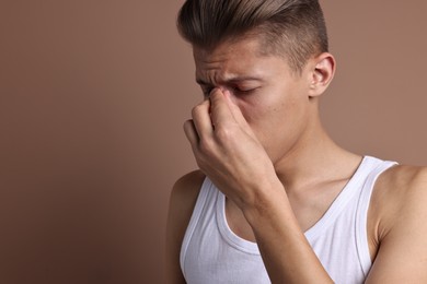 Young man suffering from sinusitis on light brown background, space for text