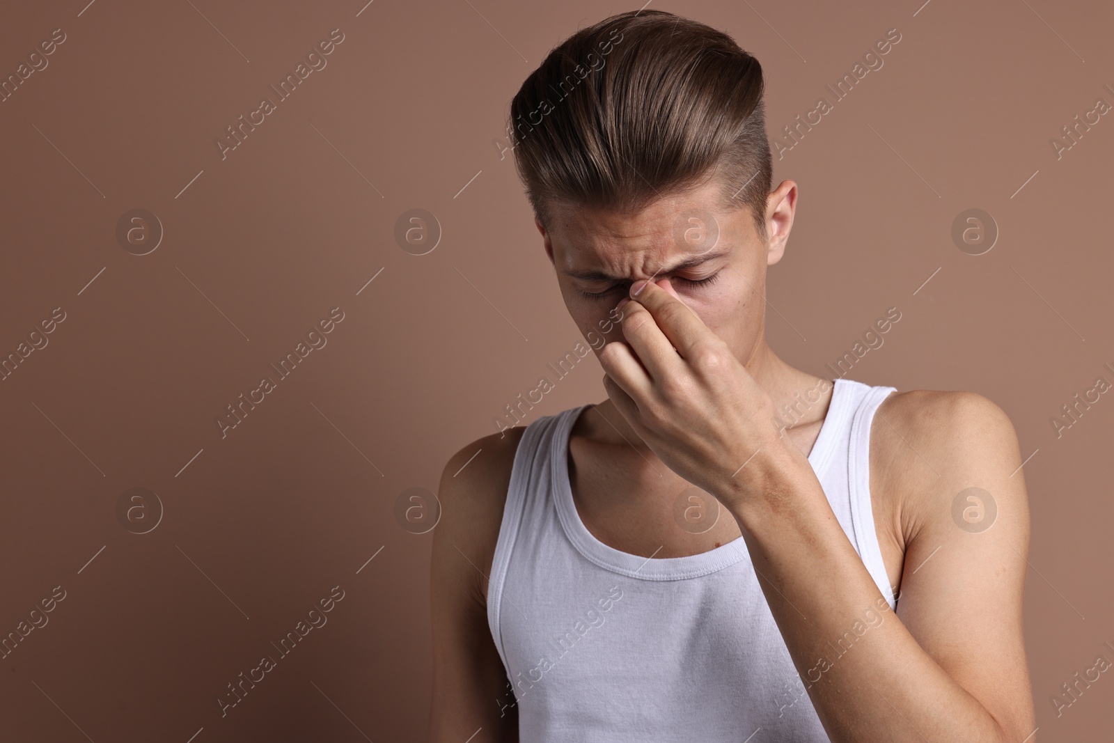 Photo of Young man suffering from sinusitis on light brown background, space for text