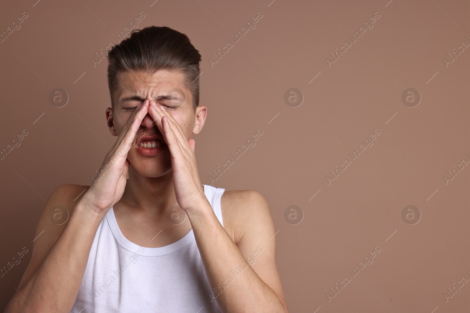 Photo of Young man suffering from sinusitis on light brown background, space for text