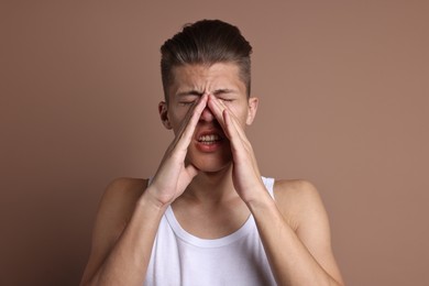 Photo of Young man suffering from sinusitis on light brown background