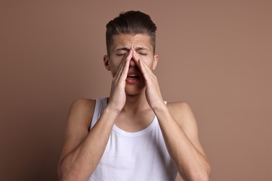 Young man suffering from sinusitis on light brown background