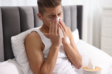 Photo of Young man with tissue suffering from sinusitis in bed at home