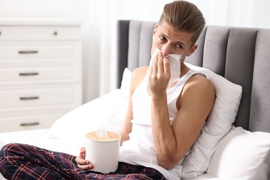 Photo of Young man with tissue suffering from sinusitis in bed at home