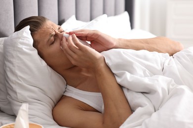 Photo of Young man with tissue suffering from sinusitis and lying in bed at home