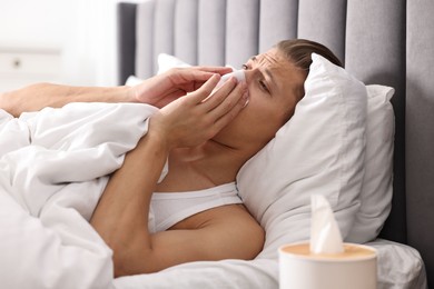 Young man with tissue suffering from sinusitis and lying in bed at home