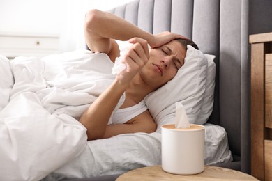 Young man with tissue suffering from sinusitis and lying in bed at home