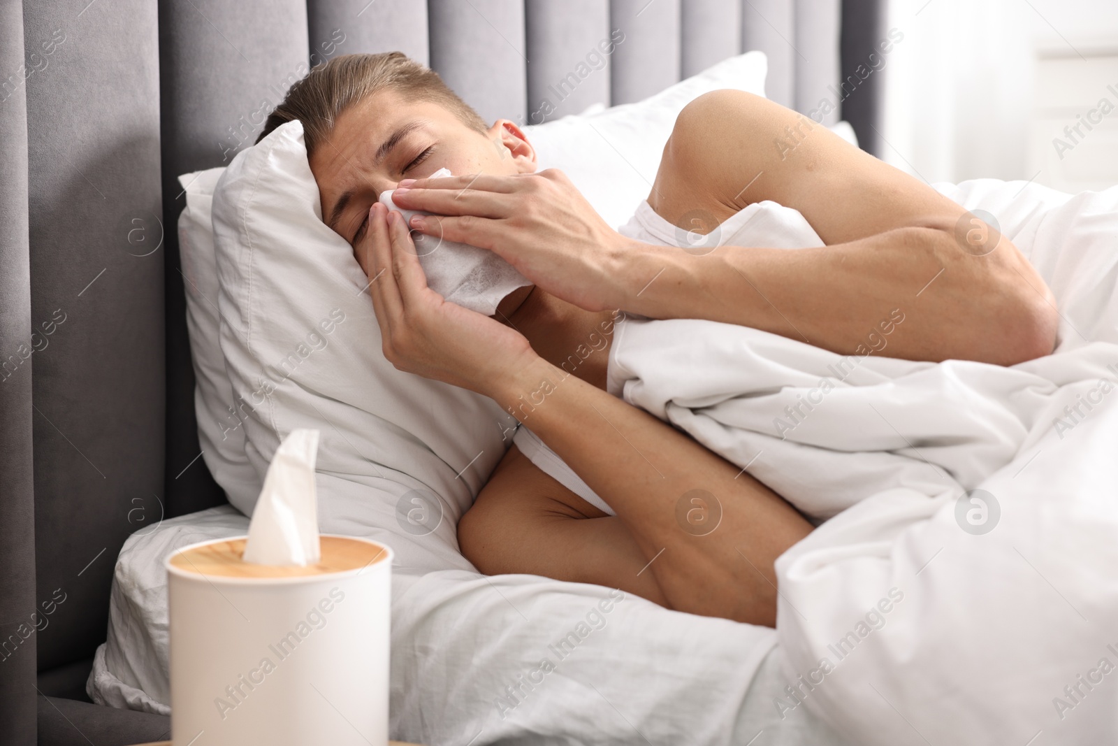 Photo of Young man with tissue suffering from sinusitis and lying in bed at home