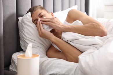 Photo of Young man with tissue suffering from sinusitis and lying in bed at home