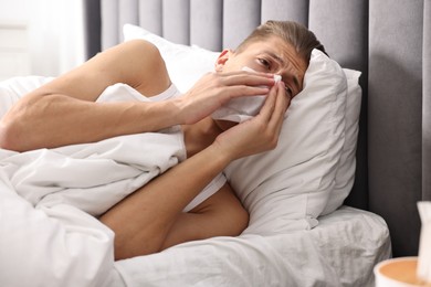 Photo of Young man with tissue suffering from sinusitis and lying in bed at home