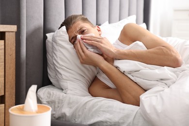 Young man with tissue suffering from sinusitis and lying in bed at home