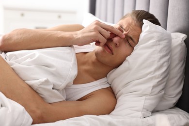 Young man suffering from sinusitis and lying in bed at home