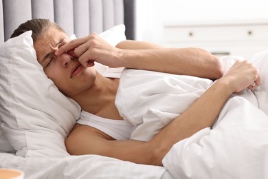 Photo of Young man suffering from sinusitis and lying in bed at home