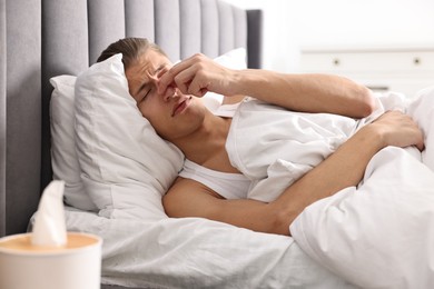 Photo of Young man suffering from sinusitis and lying in bed at home