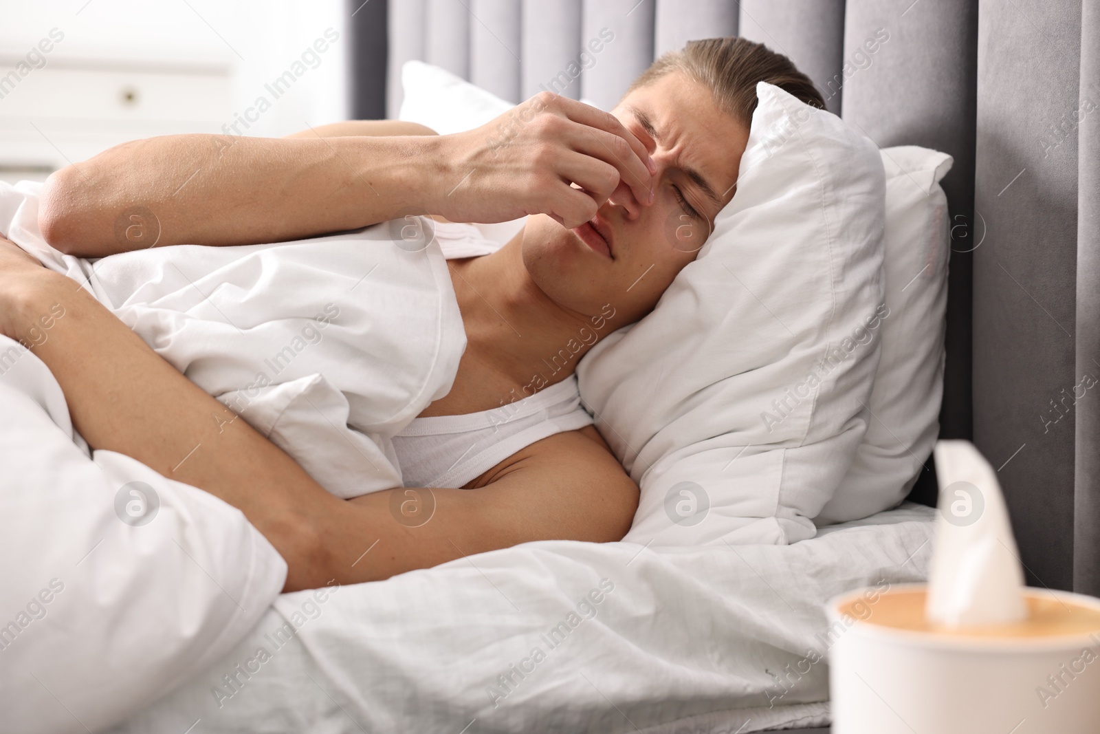 Photo of Young man suffering from sinusitis and lying in bed at home