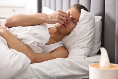 Photo of Young man suffering from sinusitis and lying in bed at home