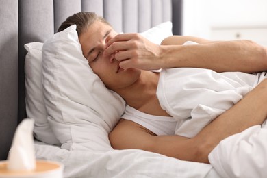 Young man suffering from sinusitis and lying in bed at home