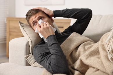 Young man with tissue suffering from sinusitis and lying in bed at home